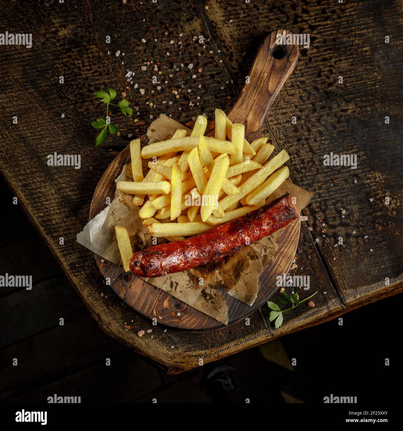 Concept de grill. Saucisse savoureuse grillée et rôtie avec frites sur l'ancienne planche à découper en bois. Banque D'Images