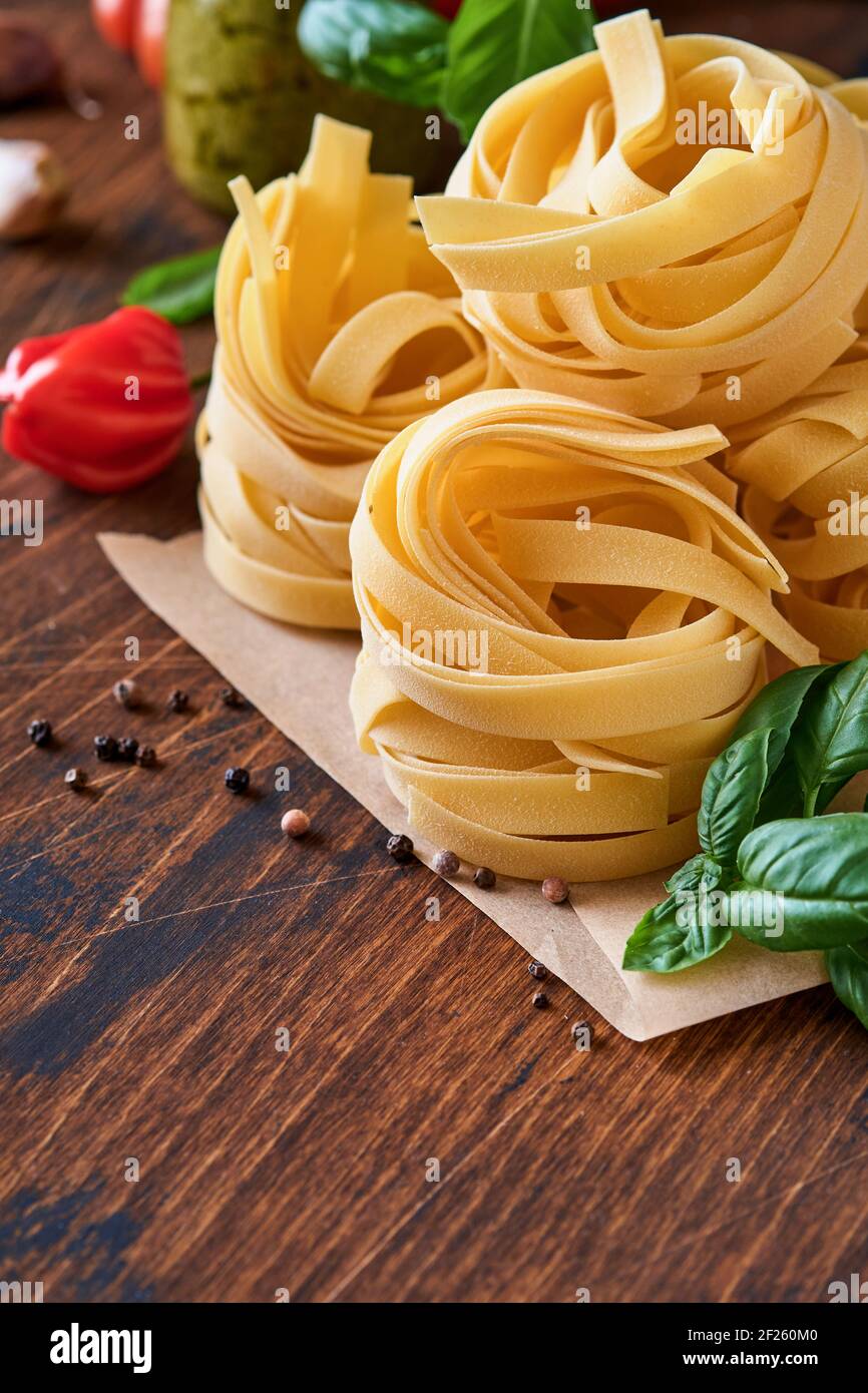 Pâtes tagliatelle maison en papier brun sur fond blanc avec huile d'olive, sause pesto, basilic et ail sur fond de table clair. Banque D'Images