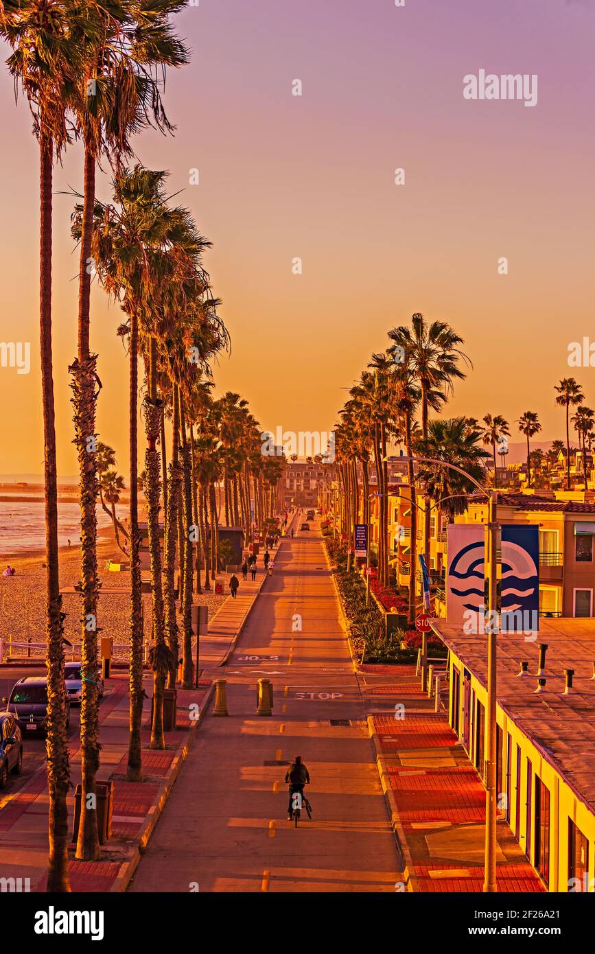 Rue de la ville longeant la plage bordée de palmiers et de touristes au coucher du soleil. Banque D'Images