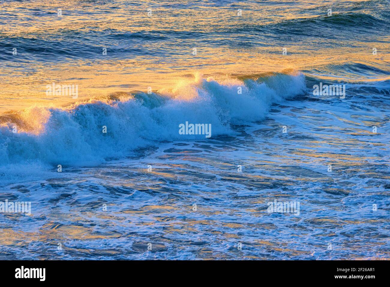 Vagues se brisant et se brisant dans l'océan avec la lumière du soleil jaune sur la surface. Banque D'Images