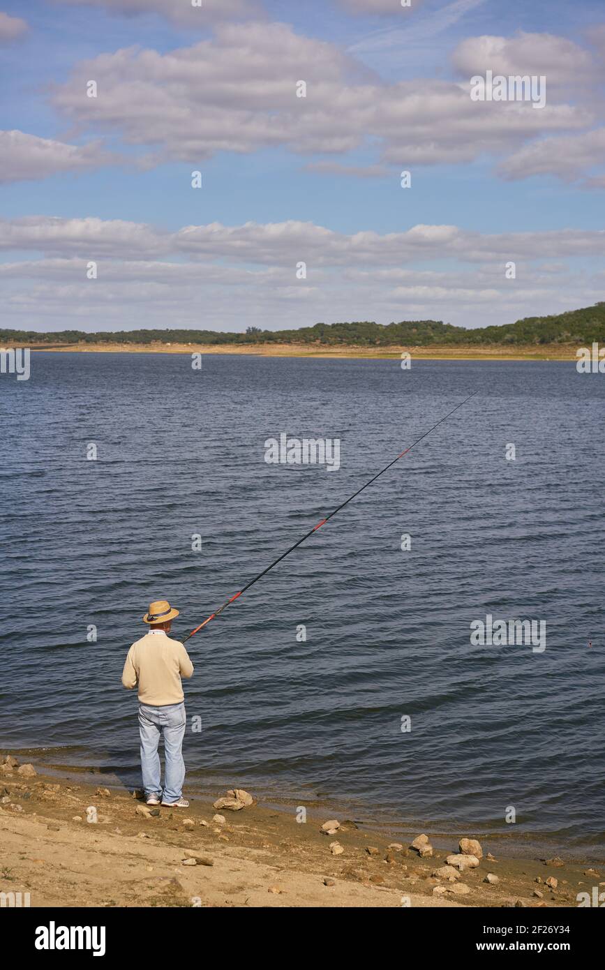 Homme âgé caucasien pêchant avec un chapeau de paille sur un barrage lac réservoir à Alentejo, Portugal Banque D'Images