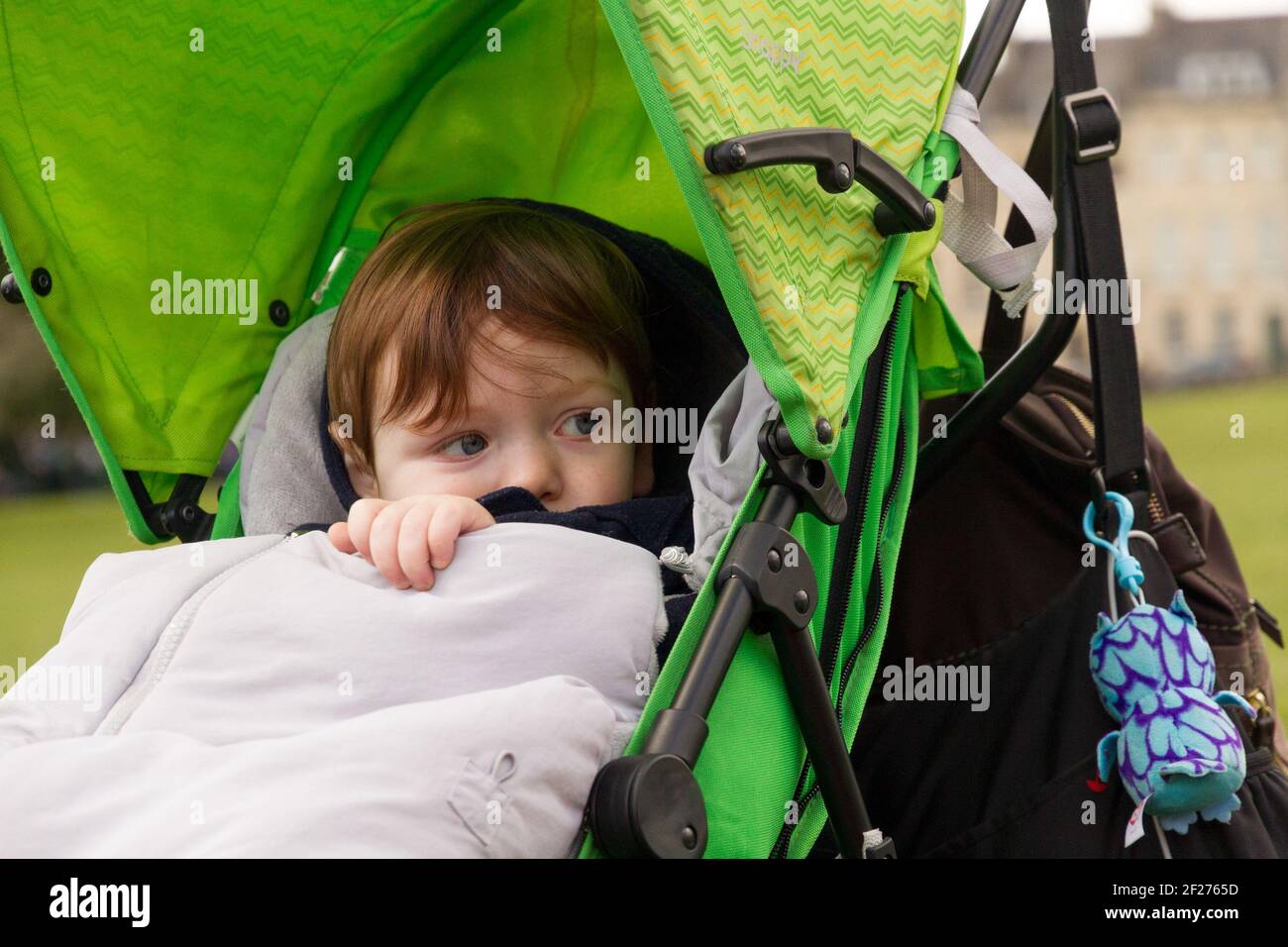 Mignon, tête rouge, bleu-eyed bébé garçon assis sur une poussette verte Banque D'Images