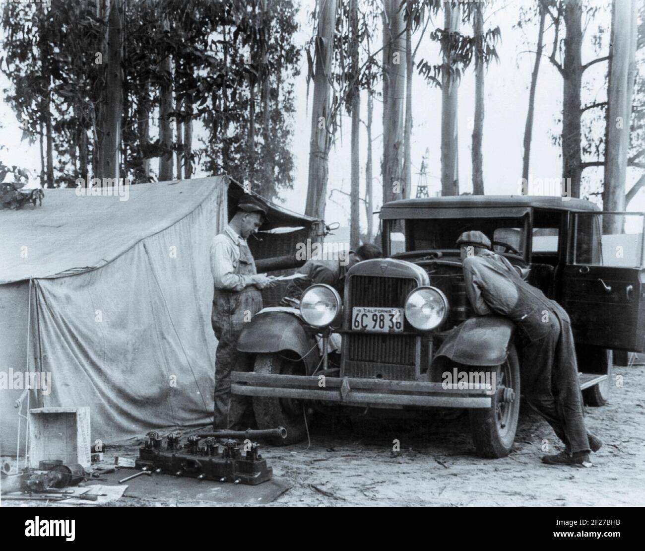 Cueilleurs de pois du Vermont - 6 semaines de gains $7.00 - au camp de squatter, Nipomo, CA. La photographie montre des hommes travaillant sur une automobile garée devant une tente dans un bosquet d'eucalyptus.24 février 1935 Photographie par Dorothea Lange Banque D'Images