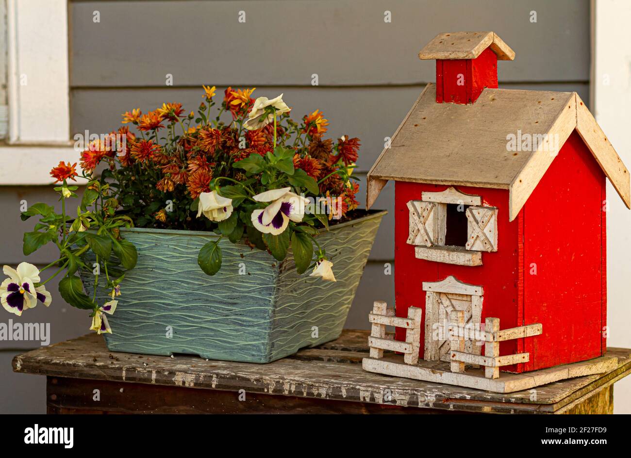 Vue rapprochée d'un modèle de maison de ferme fait main rouge placé à côté d'un pot de fleurs de pansy et de chrysanthème (maman). C'est un porche déco vintage et élégant Banque D'Images