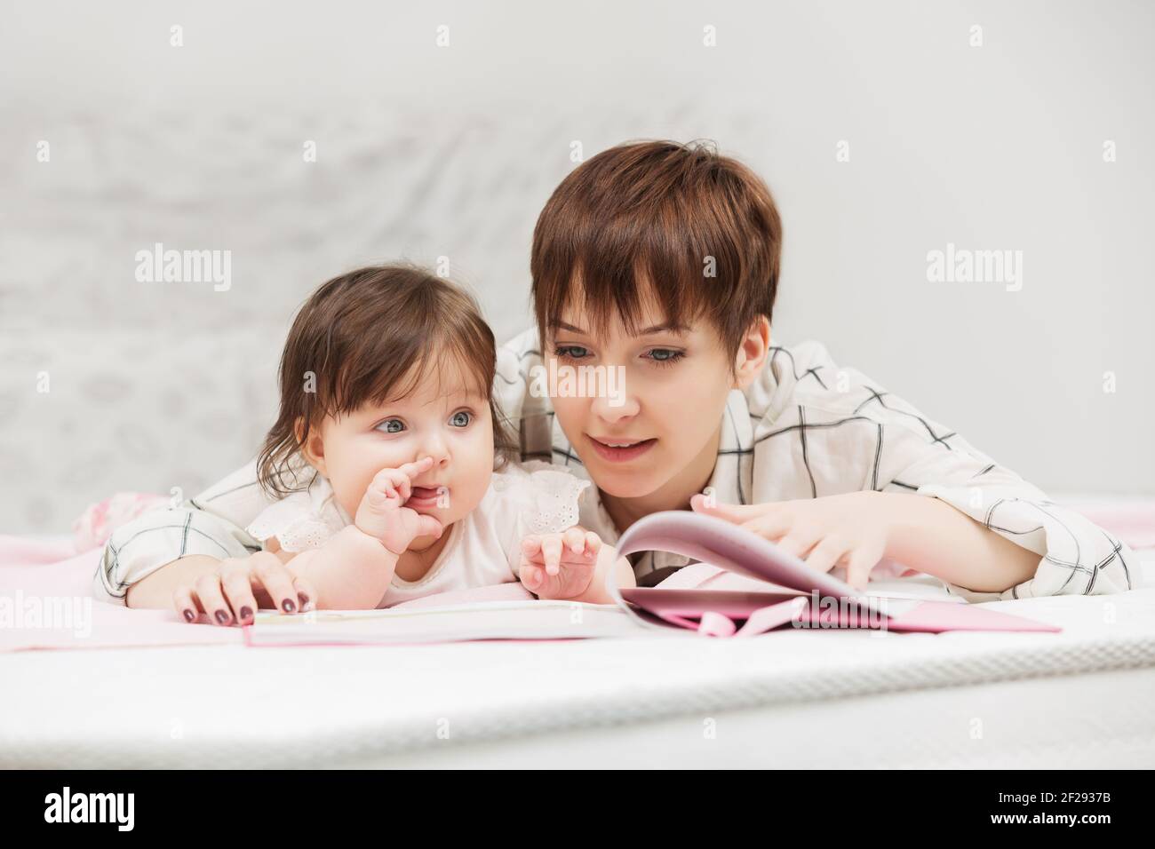 Heureux jeune mère et little baby girl reading a book on bed Banque D'Images