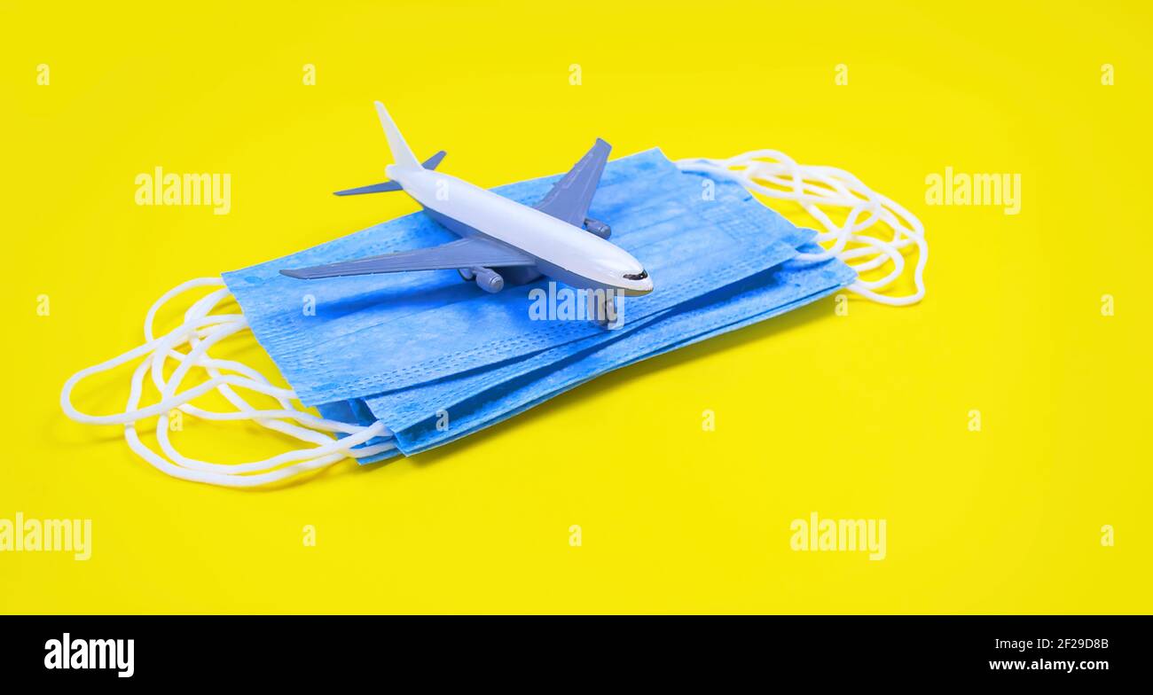 Main dans le gant tenant les avions modèle sur fond jaune. Modèle d'avion sur la main et le visage masque médical concept voyage. Copier l'espace Banque D'Images