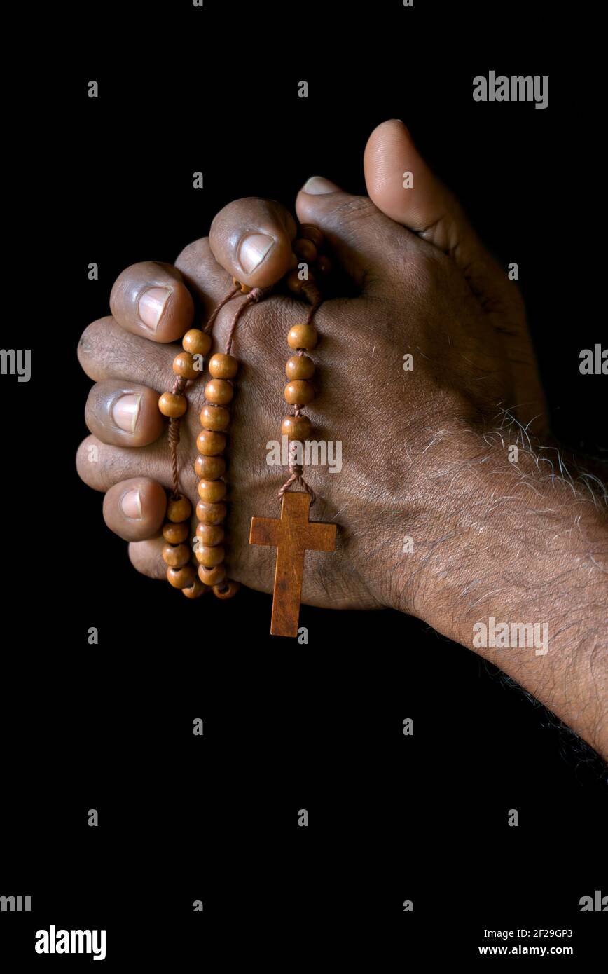 Main de prière d'un vieil homme catholique indien avec rosaire en bois isolé sur un fond noir Uni. Banque D'Images