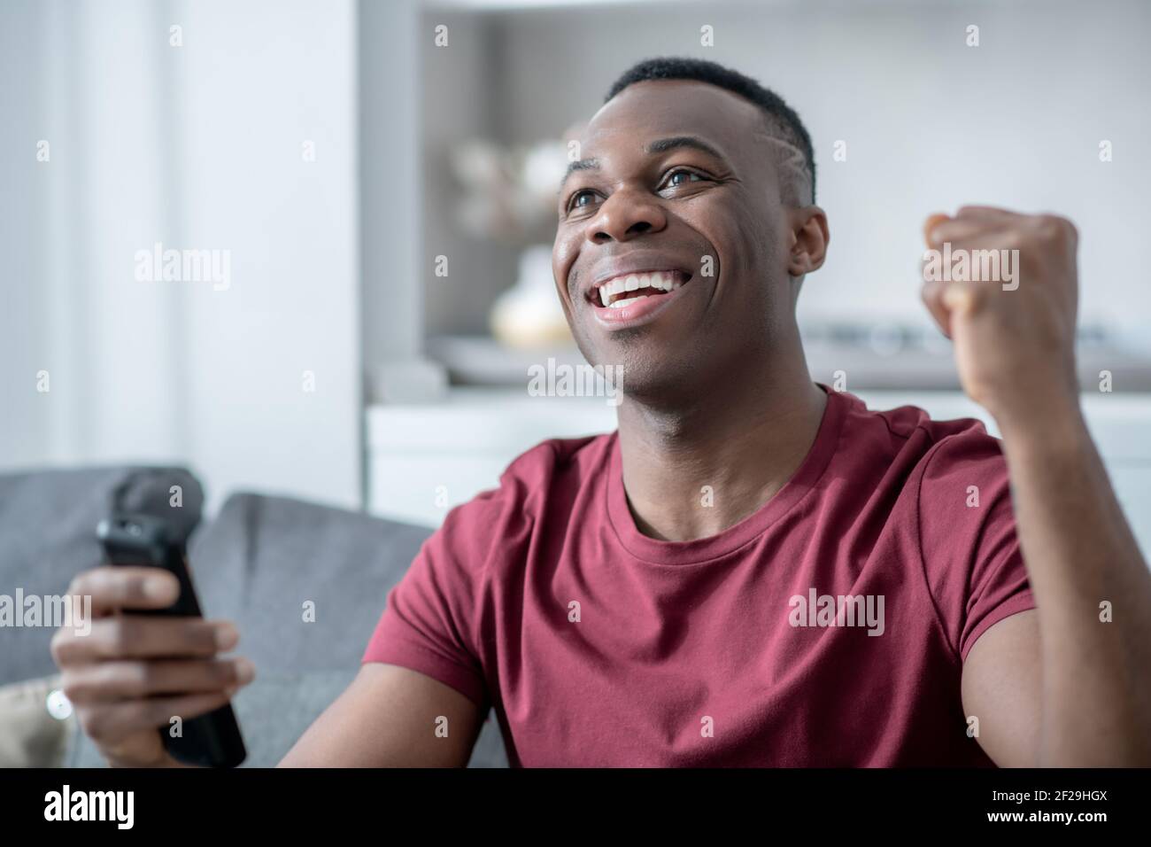 Un jeune homme à la peau sombre qui regarde la télévision et qui regarde avec enthousiasme Banque D'Images