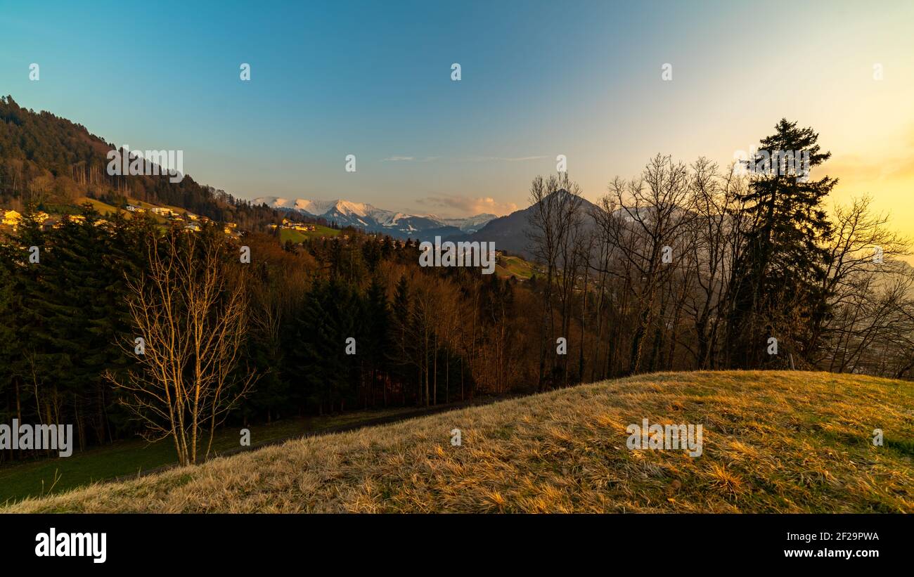 Watzenegg, Dornbirn während der goldenen Stunde mit dem verschneiten Firstgebirge und der Staufenspitze im hintergrund. Lumière du coucher de soleil au village alpin Banque D'Images