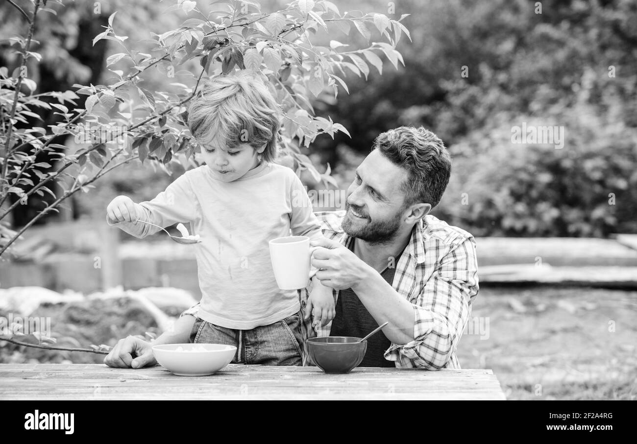 Concept de nourriture saine. Père fils manger de la nourriture et s'amuser. Menu pour enfants. Vous pourrez savourer un repas fait maison en famille. Habitudes alimentaires. Petit garçon avec papa manger nourriture pique-nique cour nature fond. Petit déjeuner d'été. Banque D'Images