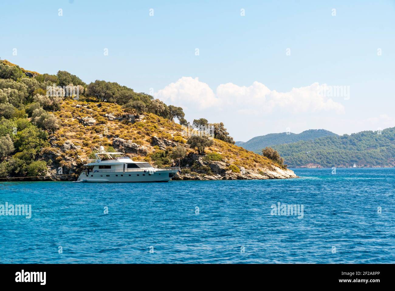 Concept d'été : bateau à yacht blanc de luxe ancré à la poupe dans une baie avec des eaux bleu turquoise. Vue de la terre avec arbres verts et mer en arrière-plan Banque D'Images