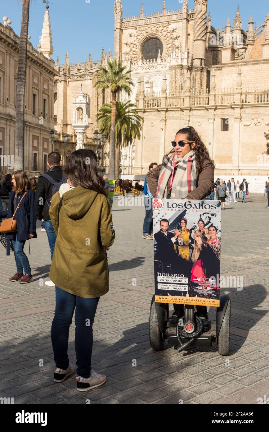 Une jeune femme sur un segway annonçant un spectacle de flamenco Aux touristes à la cathédrale Saint Marie de la Voir ou la cathédrale de Séville en Espagne Banque D'Images