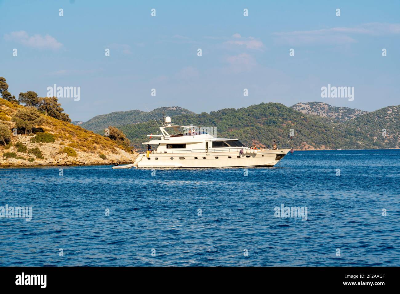 Concept d'été : bateau à yacht blanc de luxe ancré à la poupe dans une baie avec des eaux bleu turquoise. Vue de la terre avec arbres verts et mer en arrière-plan Banque D'Images