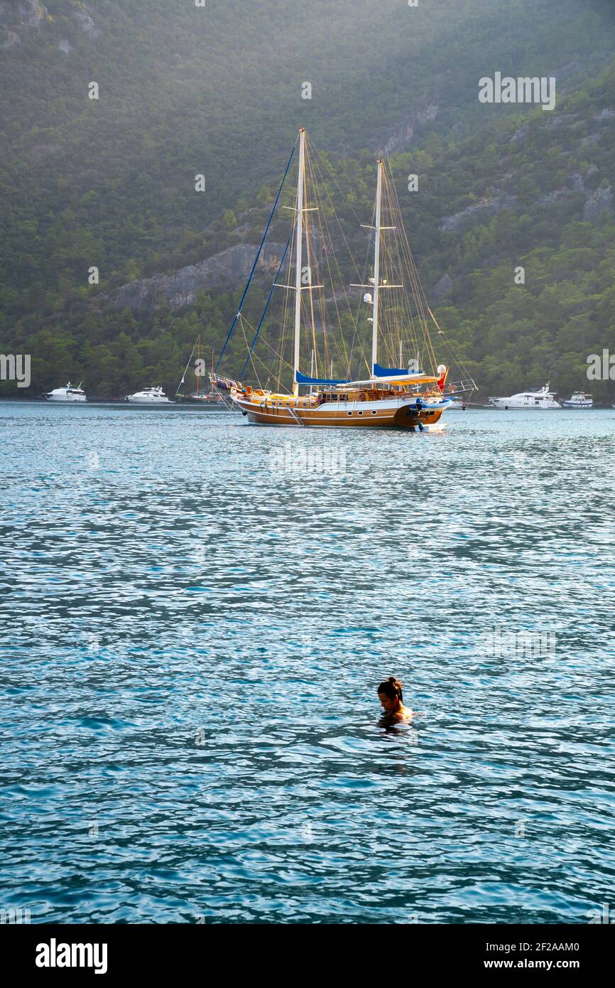 Concept d'été : un yacht turc de gullet ancré à la mer Égée avec un faisceau de soleil en arrière-plan. Une seule femme nageant dans le lac. Contraste vert - bleu Banque D'Images