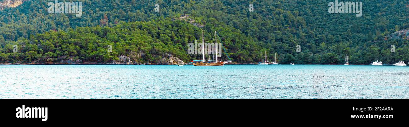 Concept d'été : un yacht turc de gullet ancré à la mer Égée avec un faisceau de soleil en arrière-plan. Photo naturelle avec espace de copie. Contraste vert et bleu Banque D'Images