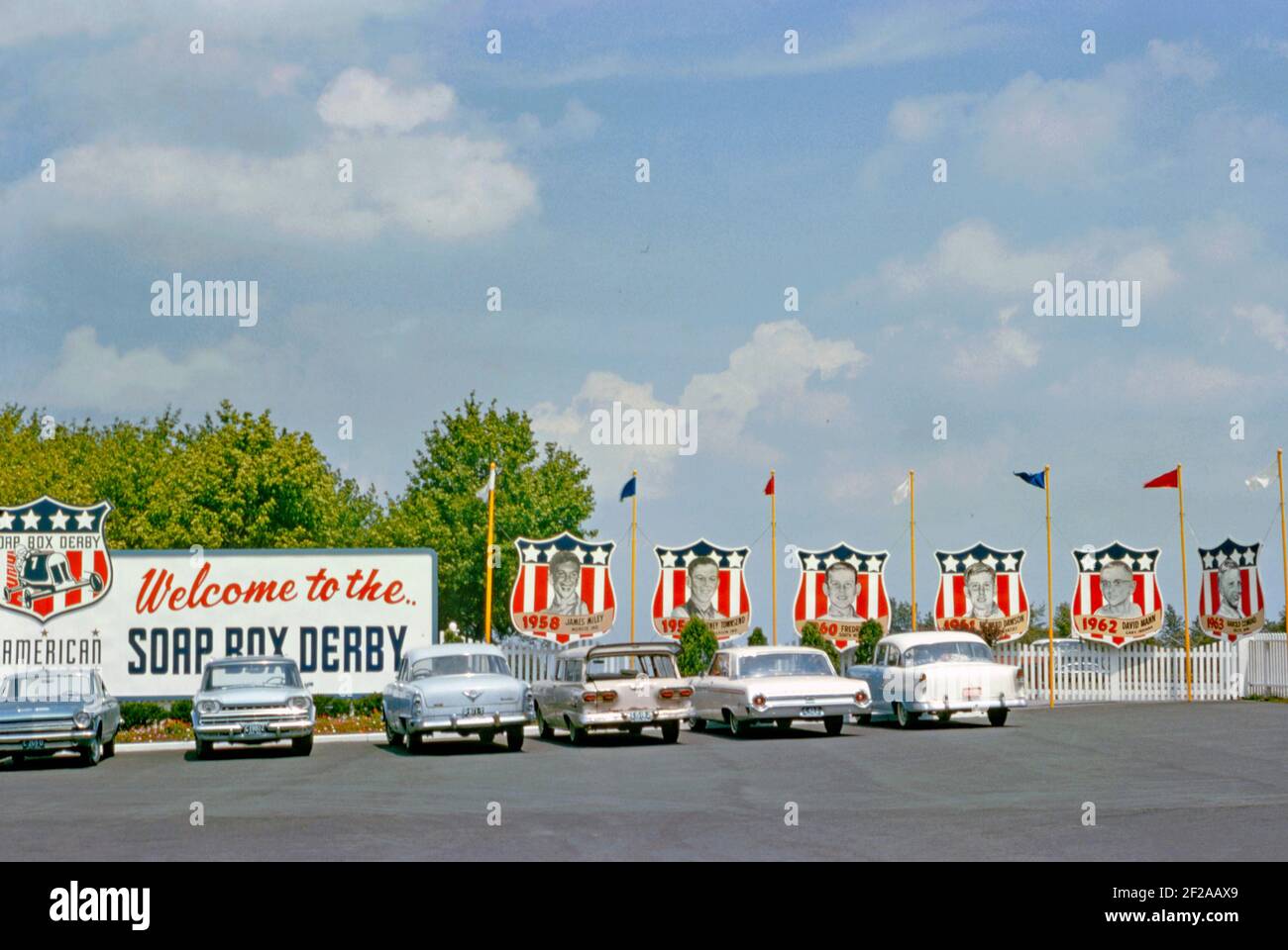 Le parking de Derby Downs, Akron, Ohio, États-Unis en 1964. Le site a été le point de départ du «All American SOAP Box Derby» depuis qu'il a été construit comme un projet d'Administration des travaux (WPA) dans les années 1930. Les traditions abondent avec un signe de bienvenue et de célèbres gagnants précédents de courses montrées sur des bannières, y compris James Miley (1958) et David Mann (1962). La piste asphaltée à trois voies commence près du sommet du George Washington Boulevard et descend en ligne droite sur la colline boisée. Cette image est tirée d'une ancienne transparence couleur Kodak amateur américaine, une photographie vintage des années 1960. Banque D'Images