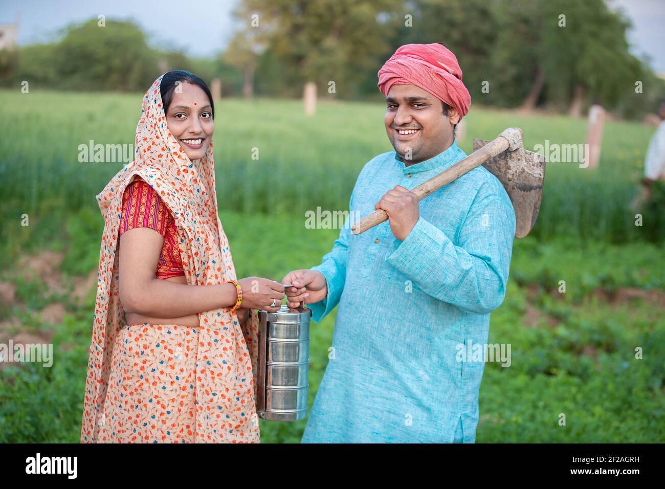Portrait d'un couple agricole indien traditionnel ou d'un ouvrier dans le champ agricole tenant une boîte à lunch de farce et un outil de pelle / pelle de jardin de queue. Banque D'Images