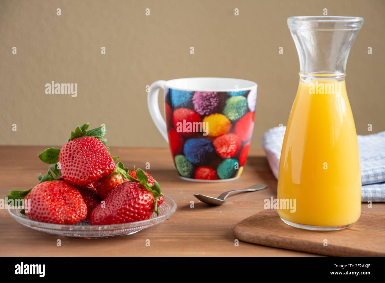 Vue sur une assiette de fraises, bouteille de jus d'orange, tasse de couleur, cuillère et tissu sur table en bois, pour le petit déjeuner, horizontal Banque D'Images