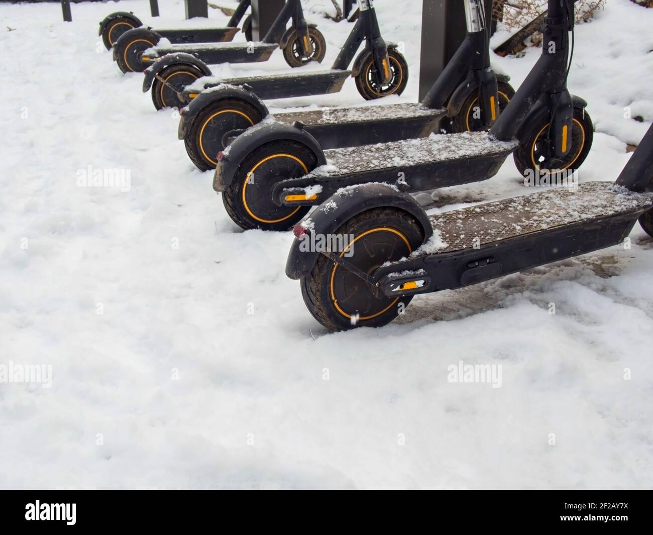 Transport urbain électrique: La rangée de lectures électriques pour monter des motos de scooter avec des accumulateurs garés dans la neige en hiver. Banque D'Images