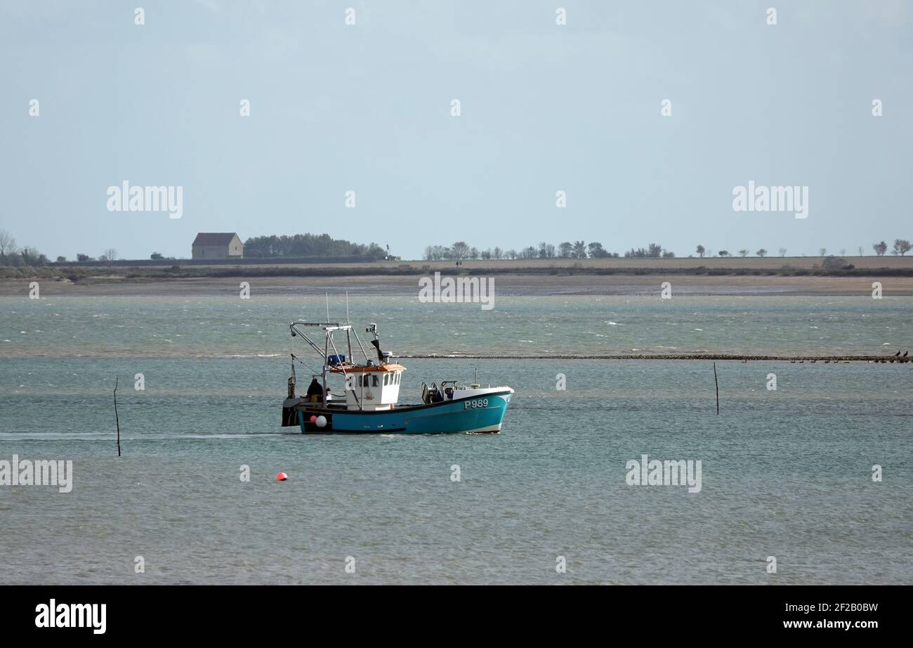 BRADWELL ON se, ROYAUME-UNI - 05 mars 2021 : un petit bateau de pêche au large de la côte de Bradwell on Sea, Essex, avec la chapelle historique de St Peter dans le b Banque D'Images