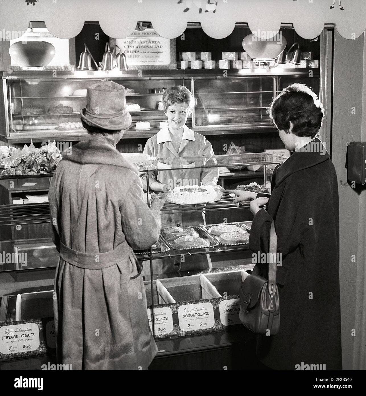 café des années 1960. Deux femmes sont debout devant le comptoir qui est plein de gâteaux et de pâtisseries fraîchement sortis du four. Suède années 60 réf. CX80-3 Banque D'Images