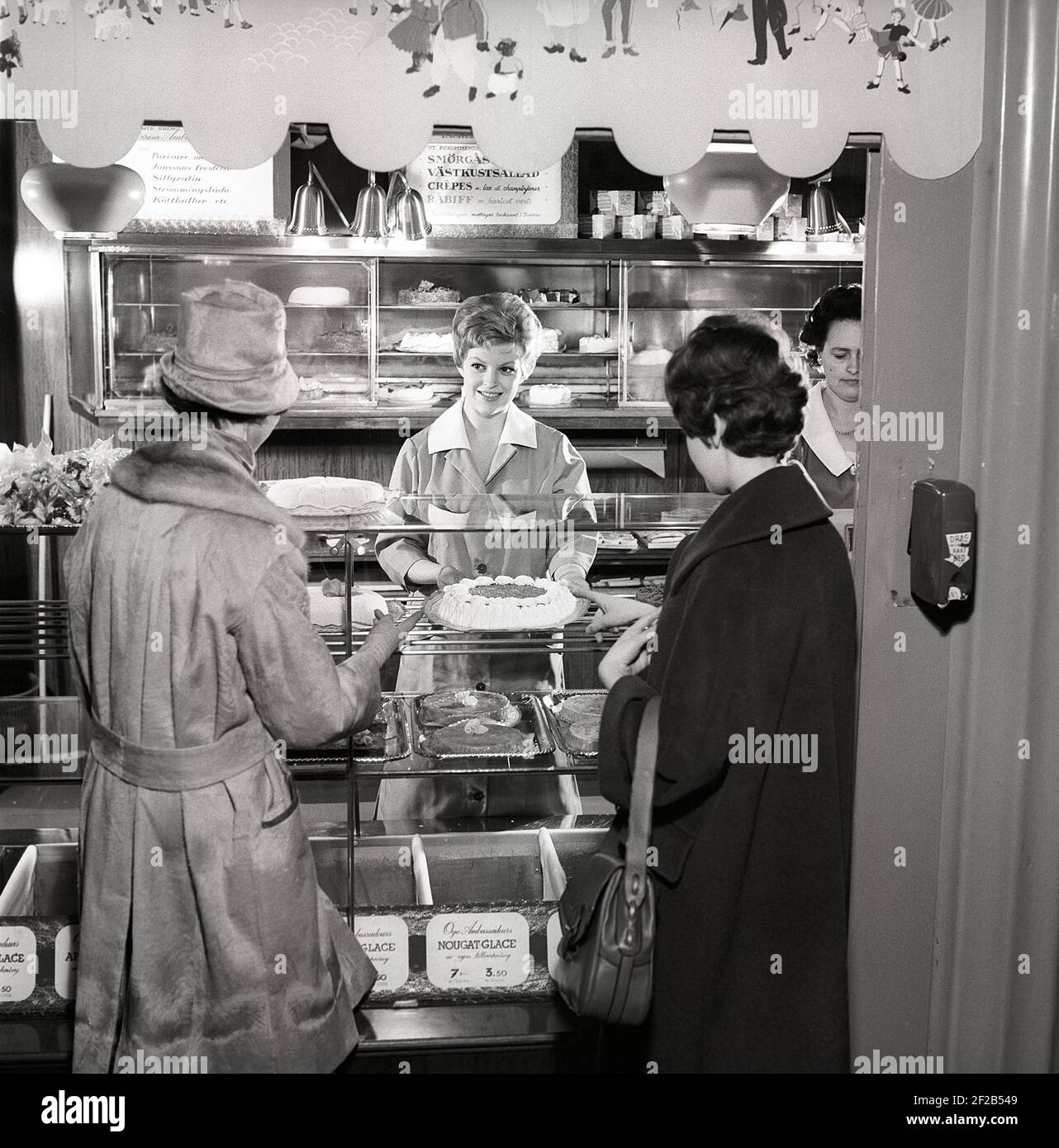 café des années 1960. Deux femmes sont debout devant le comptoir qui est plein de gâteaux et de pâtisseries fraîchement sortis du four. Suède années 60 réf. CX80-4 Banque D'Images