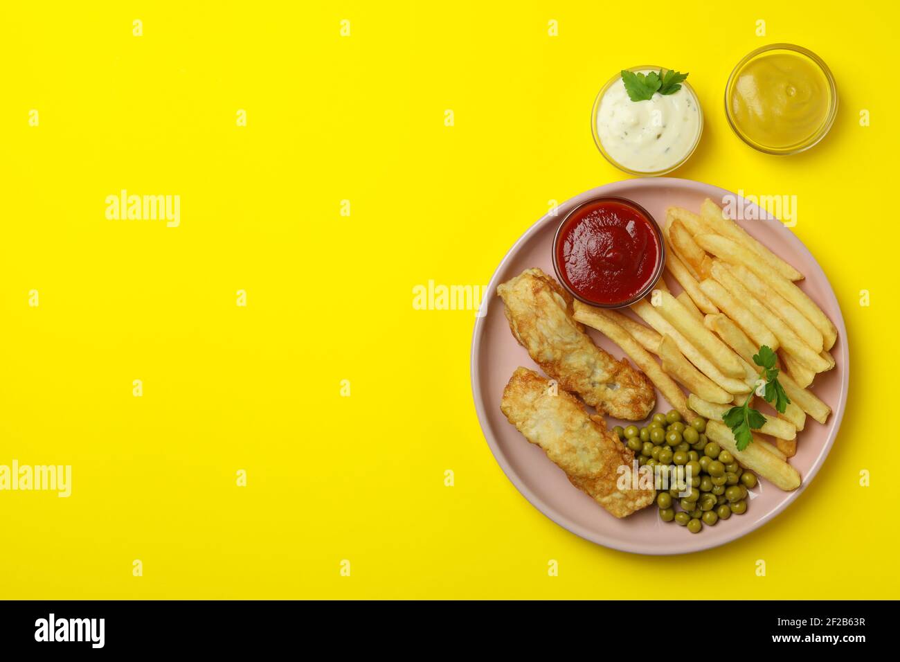Assiette de poisson frit et frites, pois et sauces sur fond jaune Banque D'Images