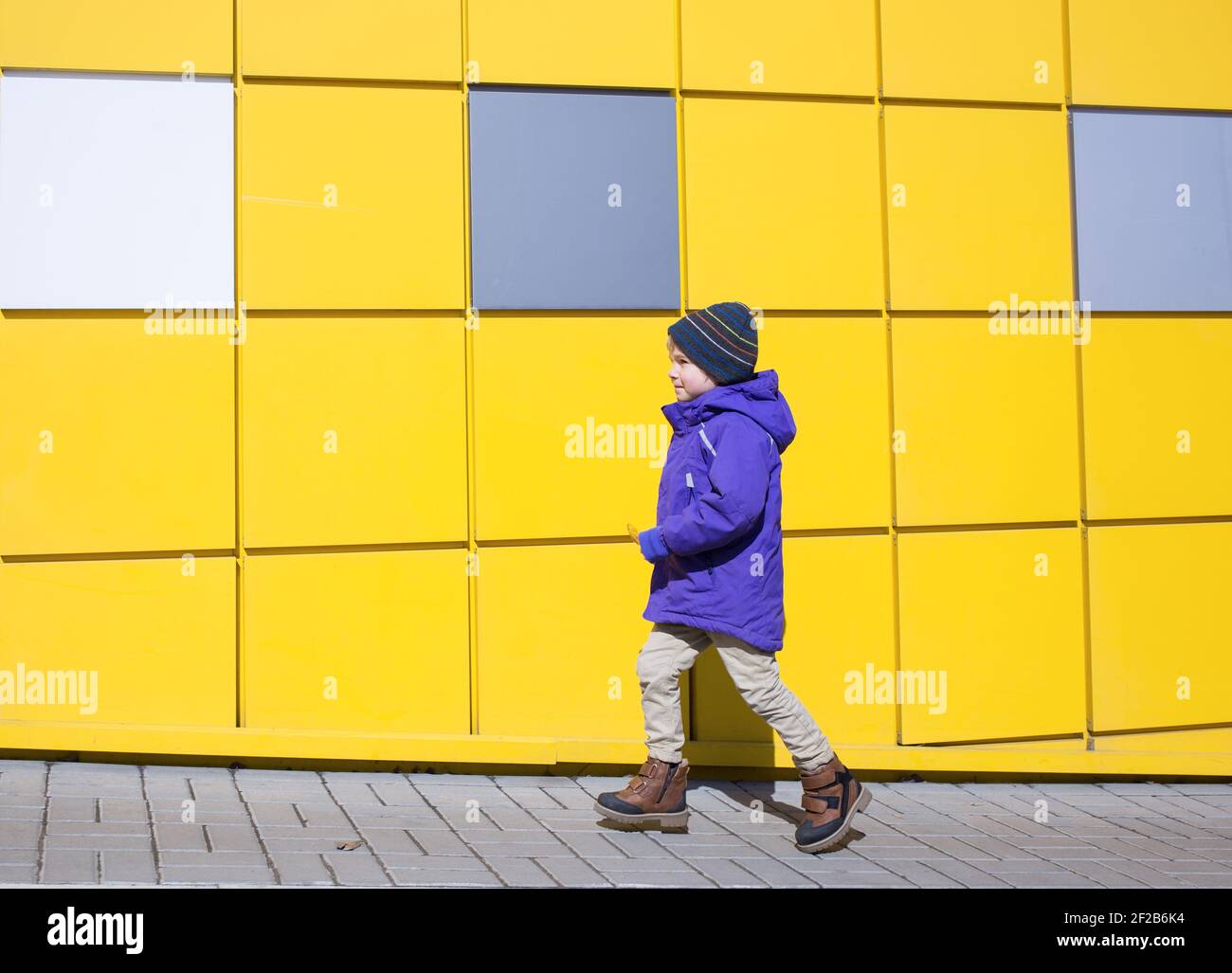 Un tout-petit garçon dans une veste violette se déplace vers l'avant le long des murs d'un mur jaune vif. Concept avancé. Positif. Charge d'énergie. Couleurs du yea Banque D'Images