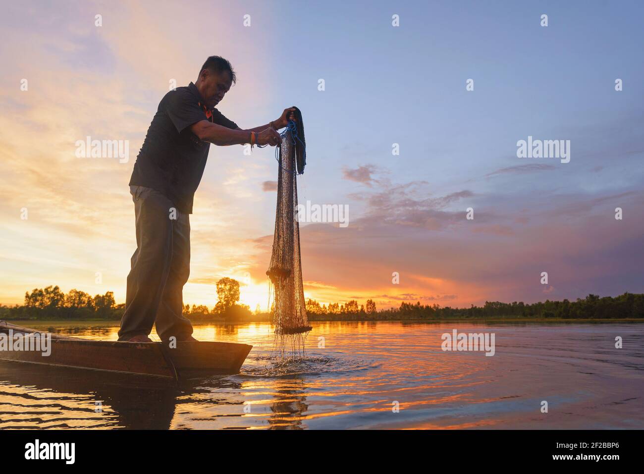 Silhouette d'un pêcheur debout dans un bateau tenant un filet de pêche au coucher du soleil, Thaïlande Banque D'Images