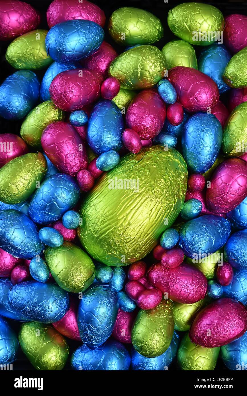Pile ou groupe de plusieurs couleurs et différentes tailles d'oeufs de pâques au chocolat enveloppés d'une feuille colorée en rose, bleu, jaune et vert lime. Banque D'Images