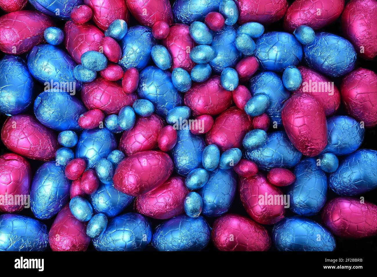 Pile ou groupe de plusieurs couleurs et différentes tailles d'oeufs de pâques au chocolat enveloppés de papier d'aluminium coloré en bleu et rose. Banque D'Images