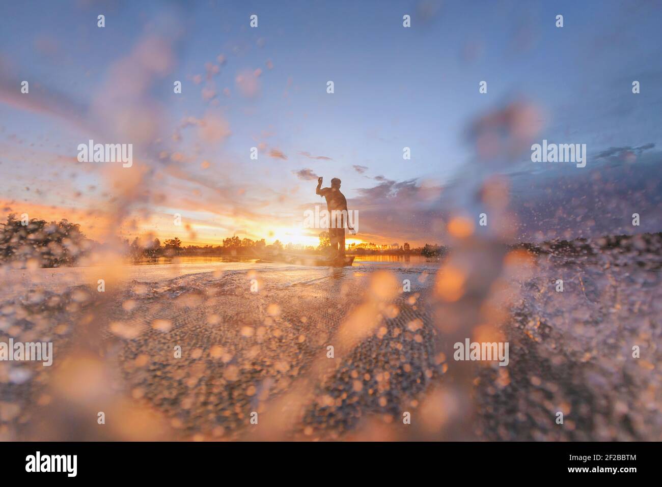 Silhouette d'un pêcheur qui jette un filet de pêche dans la rivière, Thaïlande Banque D'Images