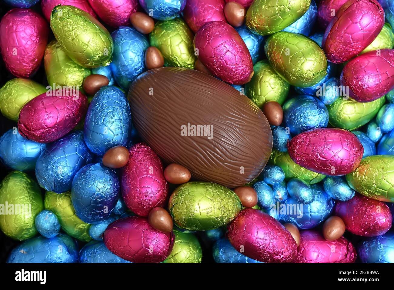 Pile ou groupe de plusieurs couleurs et différentes tailles d'oeufs de pâques au chocolat enveloppés d'une feuille colorée en bleu, rose, rouge, jaune et vert lime. Banque D'Images