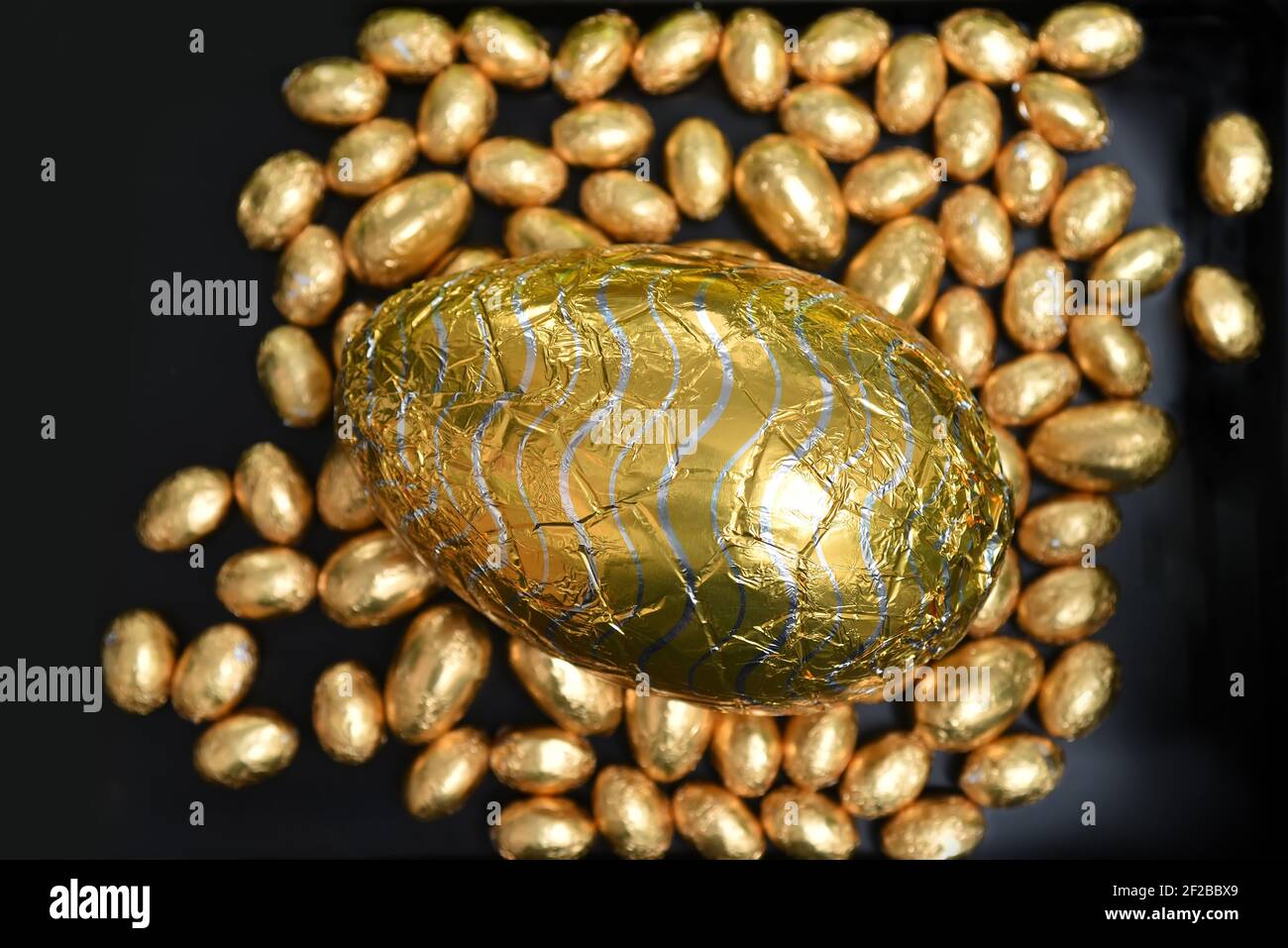 Pile ou groupe de plusieurs couleurs et différentes tailles de œufs de pâques au chocolat, enveloppés d'une feuille colorée, en or et en argent avec un grand chocolat au lait d'or Banque D'Images