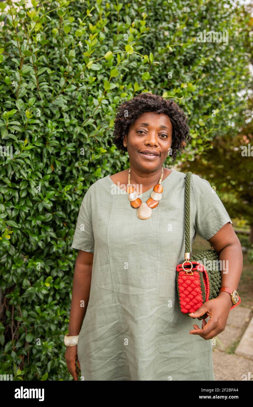 Femme africaine d'âge moyen souriant dehors avec une plante ivy en arrière-plan Banque D'Images