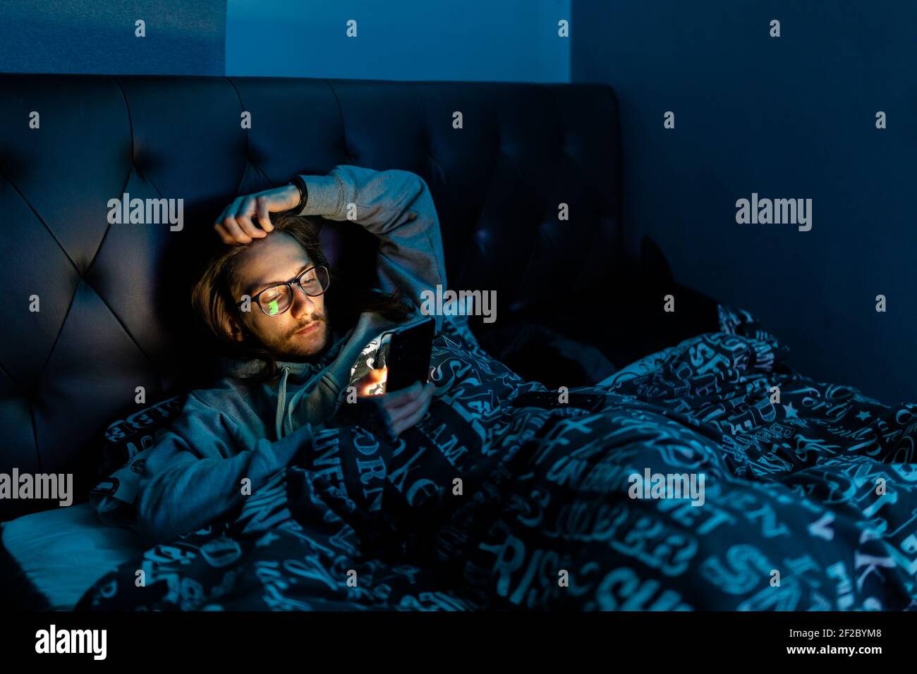 Un jeune homme accro aux médias sociaux vérifiant son téléphone avant d'aller au lit, toxicomanie, médias sociaux, après sombre concept Banque D'Images