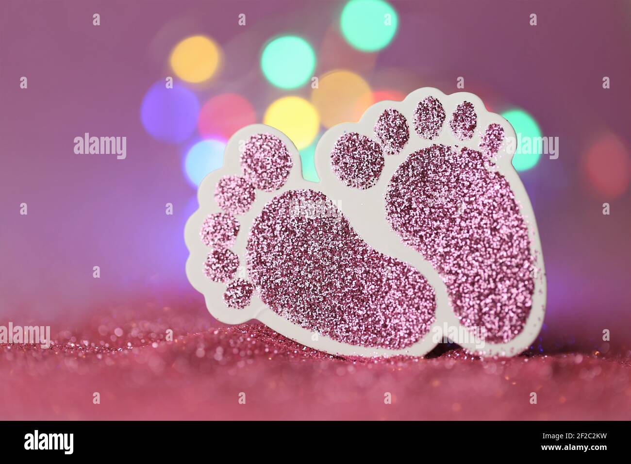 Carte de nouveau-né.la naissance d'une fille. Pieds décoratifs roses scintillants pour bébés sur fond rose pailleté avec bokeh.Baby invitation multicolore jaune Banque D'Images