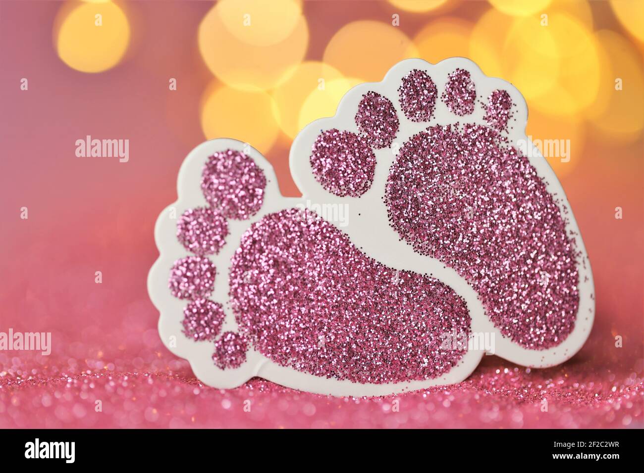 Carte de nouveau-né.la naissance d'une fille. Pieds décoratifs roses scintillants pour bébés sur fond rose pailleté avec bokeh.Baby invitation multicolore jaune Banque D'Images