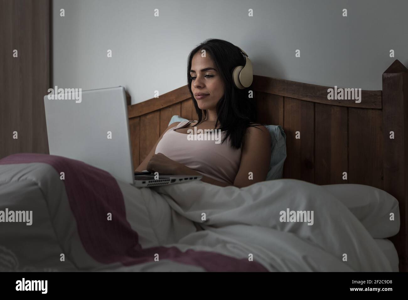 Femme indépendante assise sur un lit sous une couverture et travaillant sur projet à distance tout en naviguant sur un netbook dans la chambre Banque D'Images