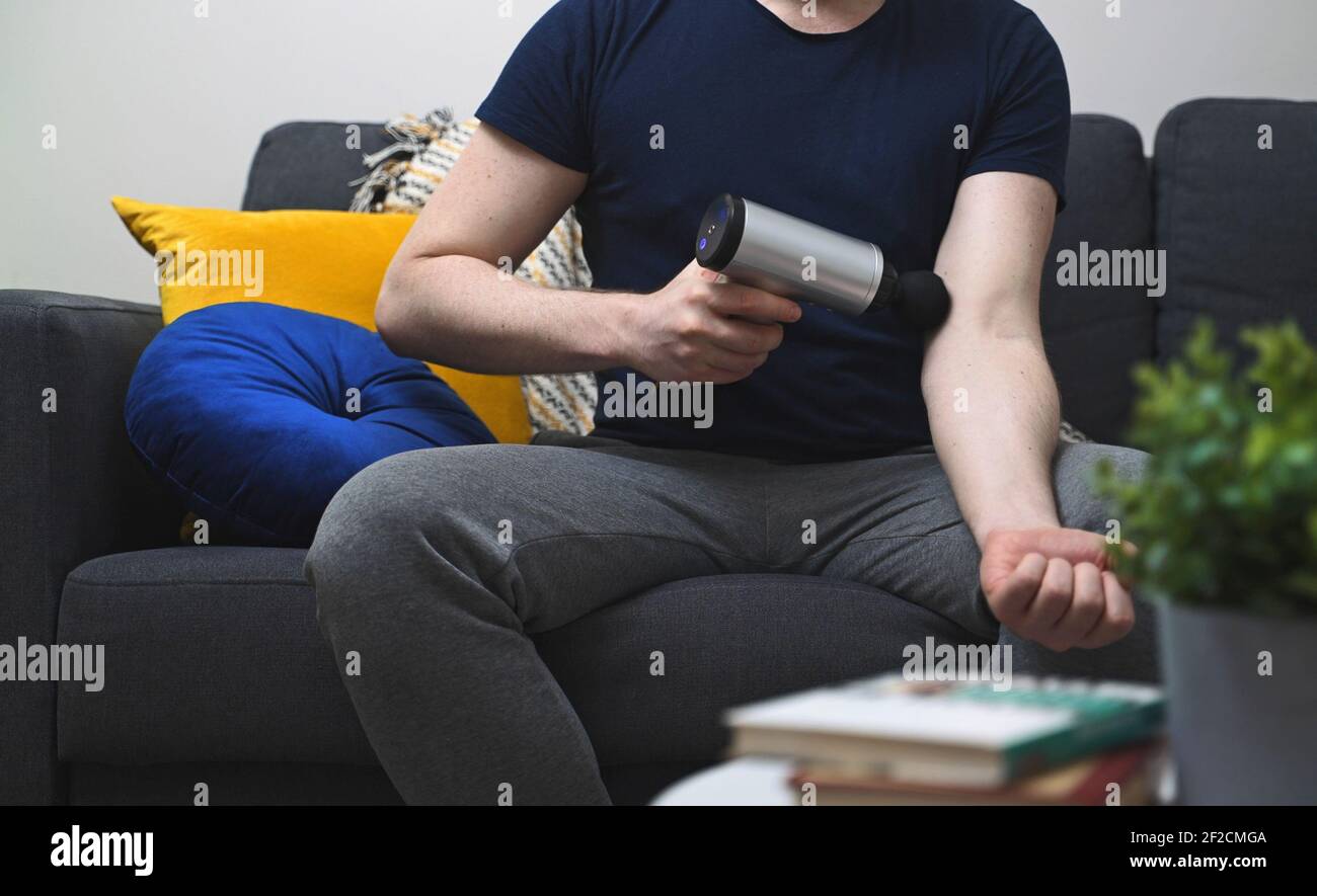 Homme massant le bras avec dispositif de percussion de massage à la maison. Banque D'Images