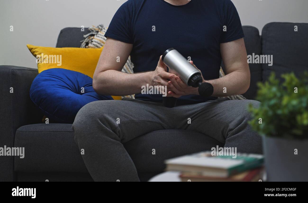 Homme avec appareil de massage à percussion à la maison. Banque D'Images