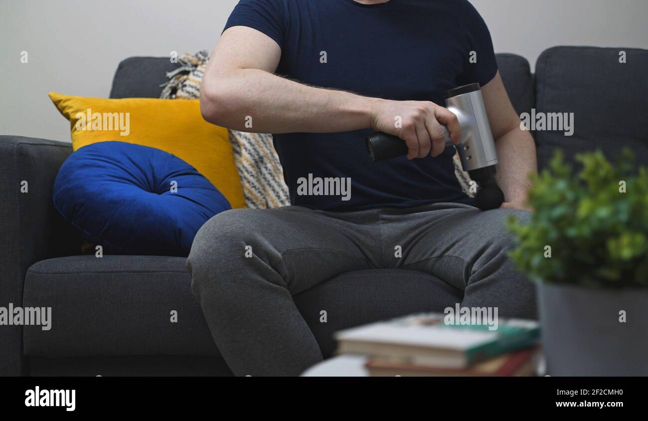 Homme massant la jambe avec dispositif de percussion de massage à la maison. Banque D'Images