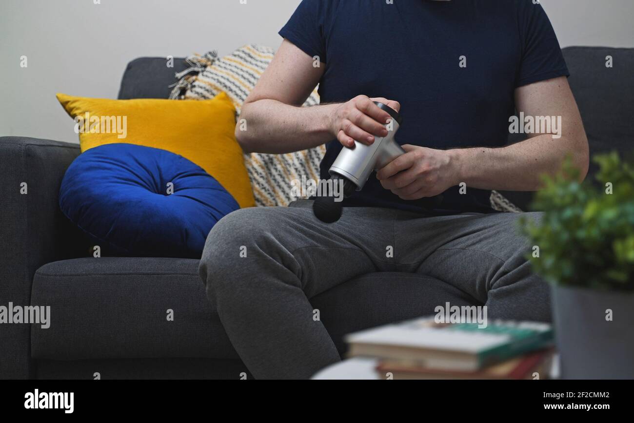 Homme avec appareil de massage à percussion à la maison. Banque D'Images