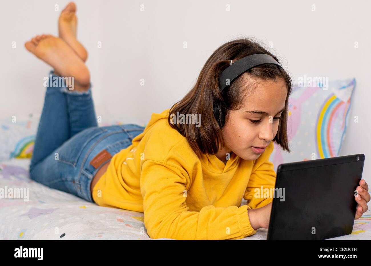 Petite fille caucasienne, avec un plâtre moulé dans une main, portant un  sweat-shirt jaune et un Jean, pieds nus, à l'écoute de la musique très  heureuse, avec sans fil Photo Stock -