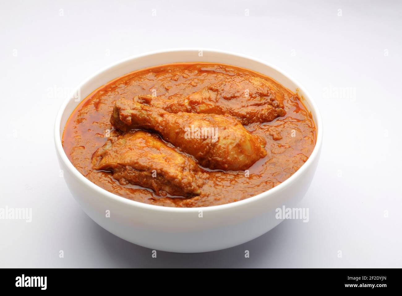 Curry de poulet ou masala, curry de poulet épicé fait à la noix de coco frite de manière traditionnelle, arrangé dans un bol en céramique blanc avec fond blanc, isola Banque D'Images