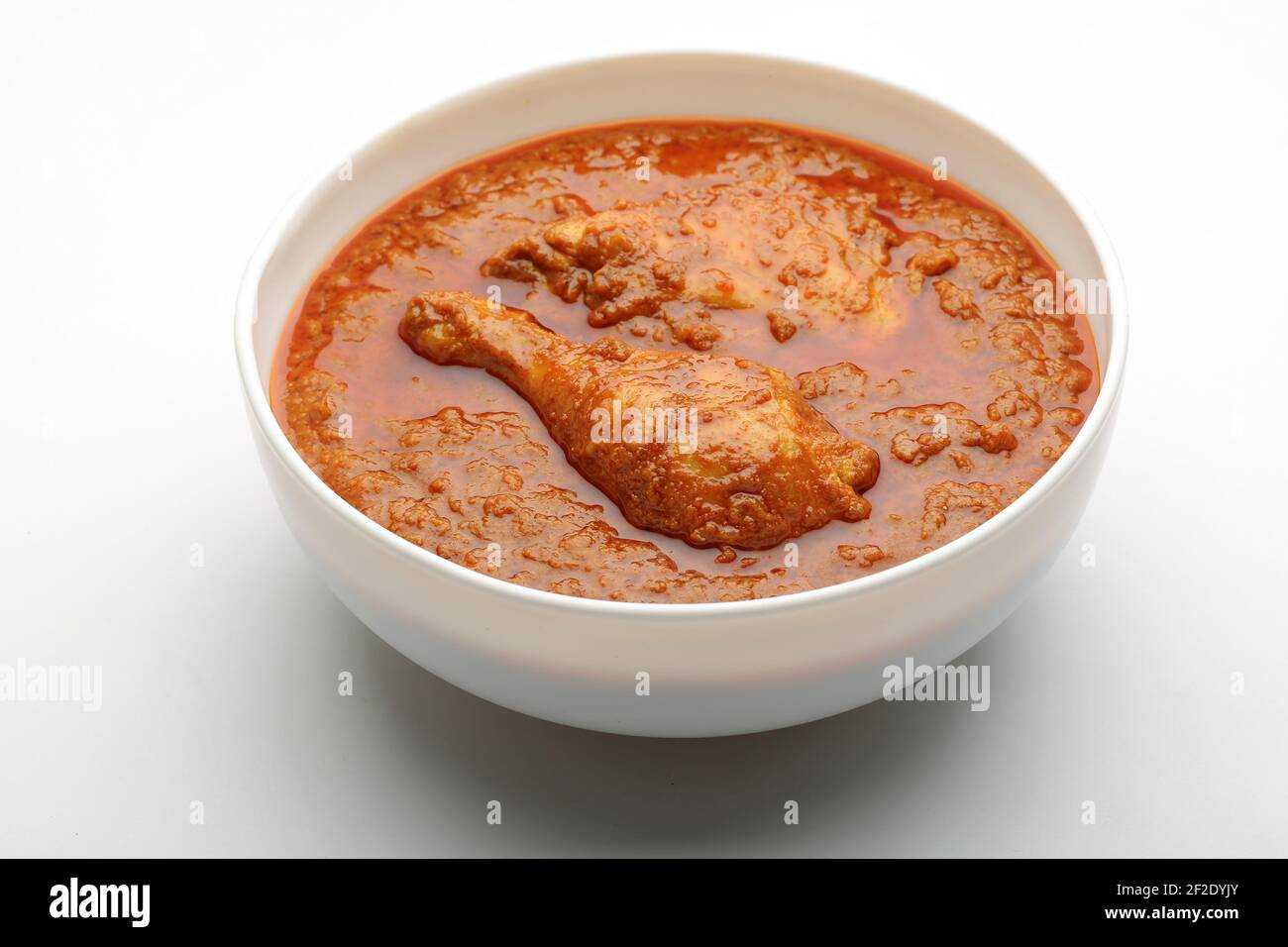 Curry de poulet ou masala, curry de poulet épicé fait à la noix de coco frite de manière traditionnelle, arrangé dans un bol en céramique blanc avec fond blanc, isola Banque D'Images