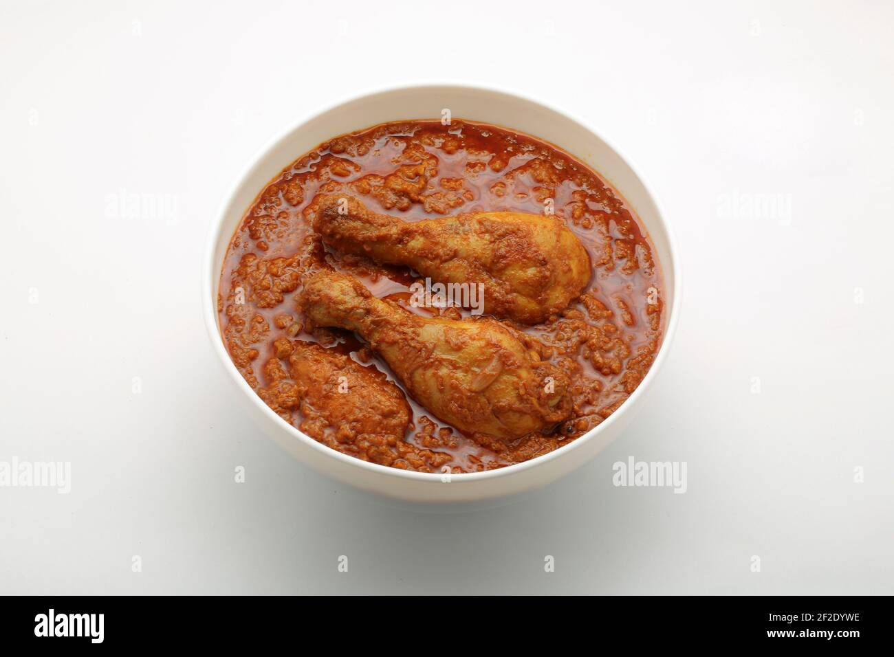 Curry de poulet ou masala, plat piquant de poulet rouge épicé garni de feuilles de coriandre et de piment vert frais qui est disposé dans un cera blanc Banque D'Images