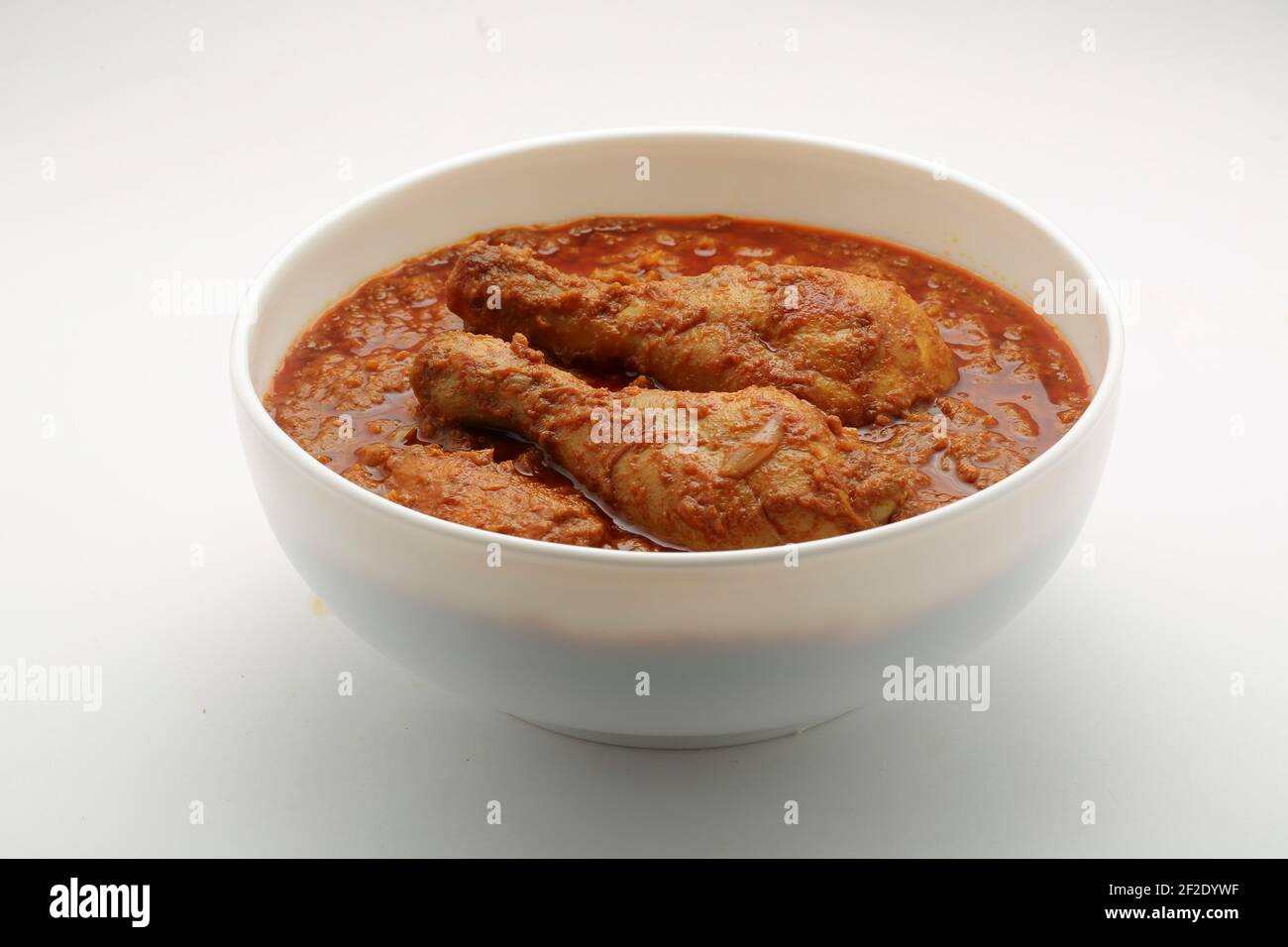 Curry de poulet ou masala, plat piquant de poulet rouge épicé garni de feuilles de coriandre et de piment vert frais qui est disposé dans un cera blanc Banque D'Images