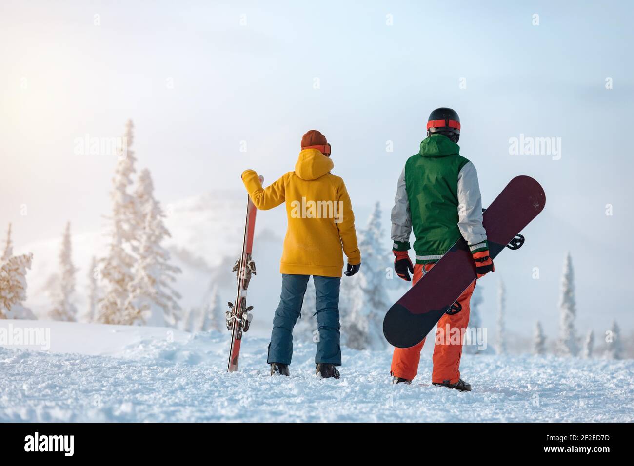 Le skieur femelle et le snowboardeur mâle sont debout sur fond de montagne enneigée au coucher du soleil. Concept de station de ski Banque D'Images