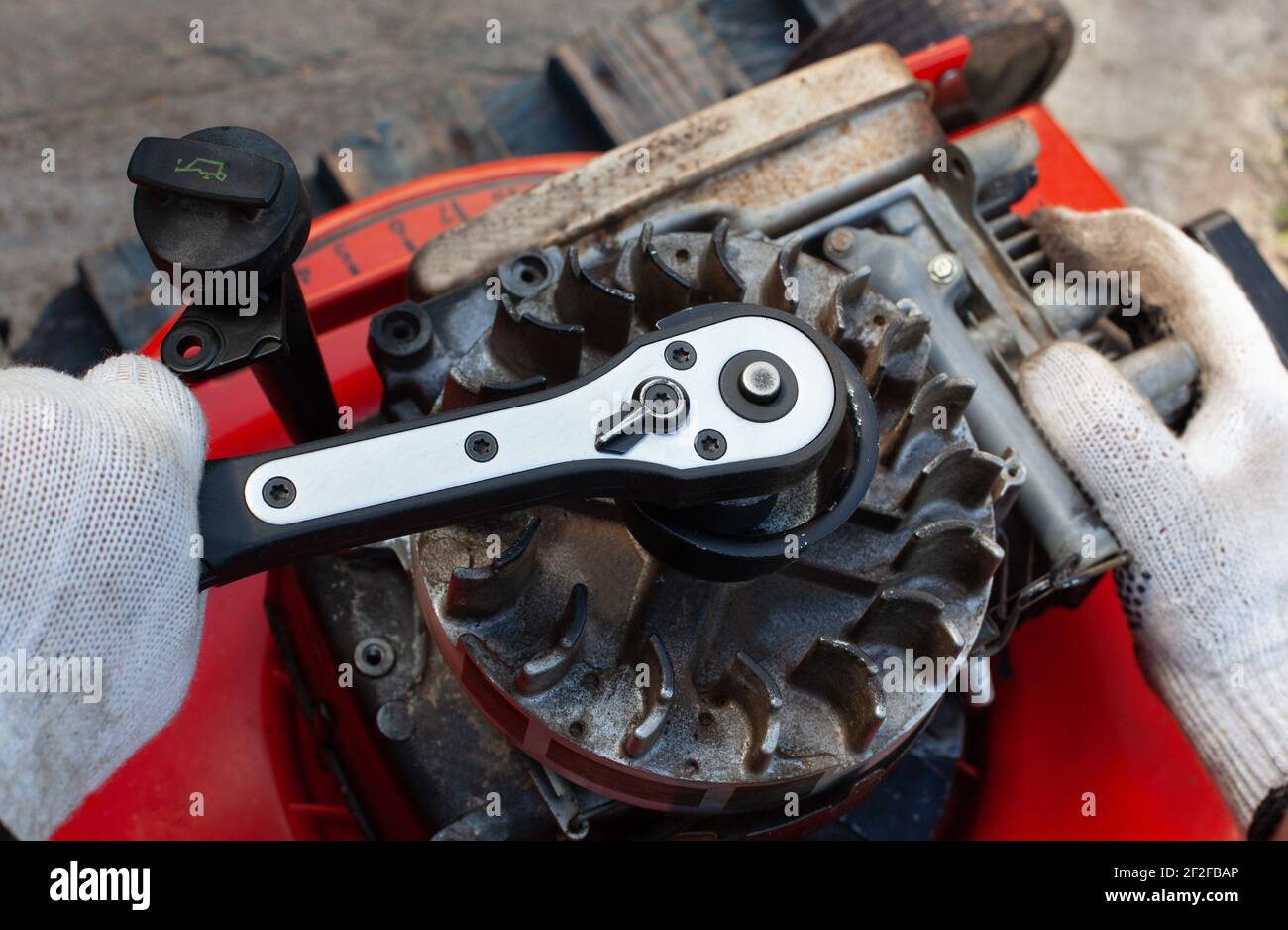 L'homme répare la tondeuse dans le garage. Il serre la bougie. Banque D'Images